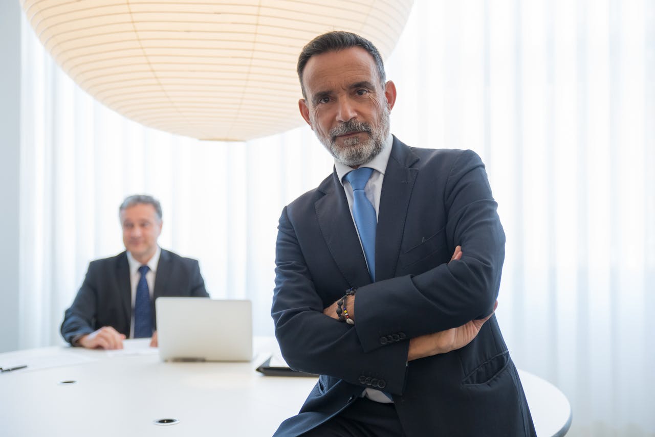 Two businessmen in suits, confidently posing in a modern office setting with a bright, professional atmosphere.